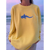 Person wearing a yellow sweatshirt with a blue shark design on a beach